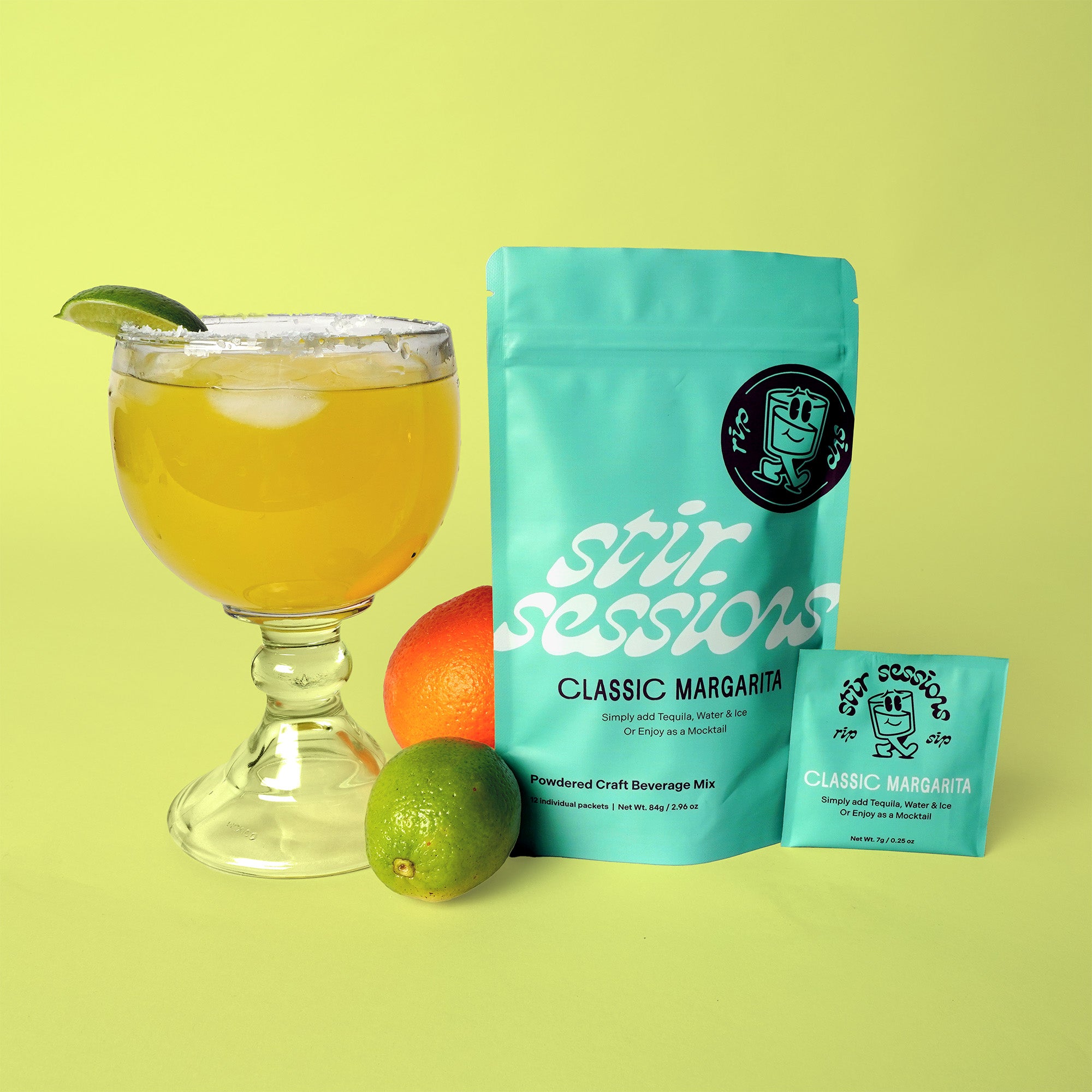 Glass of margarita with lime and orange, next to 'Stir Sessions' Classic Margarita mix on a yellow background