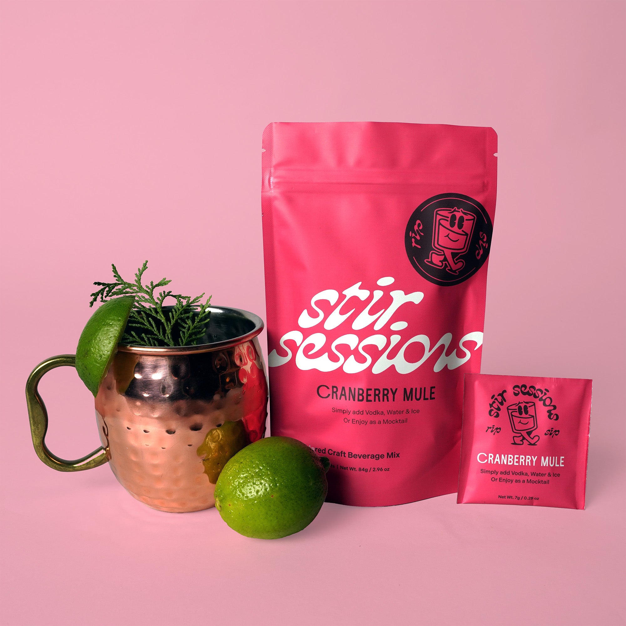 Stir Sessions Cranberry Mule powdered cocktail or mocktail drink beverage packaging with a copper mug and limes on a pink background