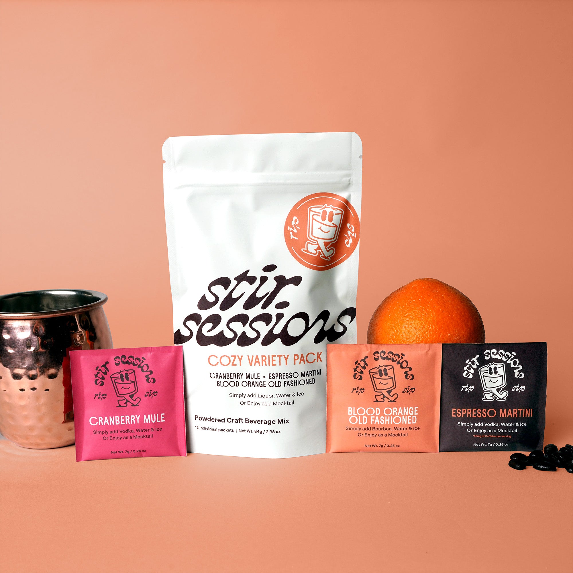 Stir Sessions Cozy Variety Pack of powdered craft cocktail or mocktail beverage mixers with a copper mug and oranges on a peach background. 