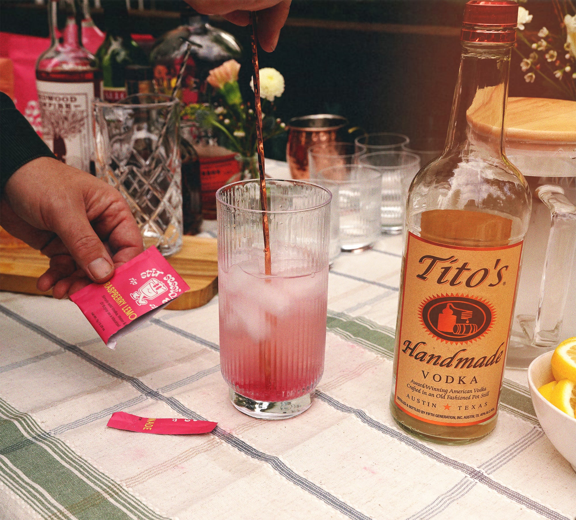 Preparing a Stir Sessions Raspberry Lemonade powdered cocktail or mocktail beverage with Tito's Handmade Vodka on a table. 